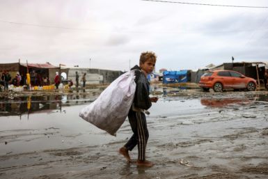 A displaced Palestinian child carrying a bag walks barefoot in a displacement camp in the central Gaza Strip