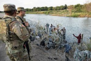 Members of the Texas National Guard look on as migrants try to find a way past razor wire in Eagle Pass, Texas