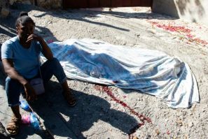 A woman sits next to the body of her brother, who was killed by alleged members of an armed gang in Petion-Ville, a suburb of Port-au-Prince, Haiti
